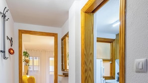 Un pasillo con una silla amarilla, una puerta de madera y una zona de cocina con armarios y un fregadero.