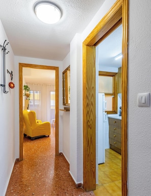 A hallway with a yellow chair, a wooden door, and a kitchen area with cabinets and a sink.