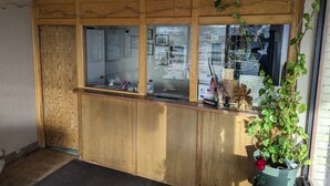 Un mostrador de recepción con diseño de paneles de madera, un ventanal de vidrio y una planta en maceta.