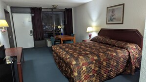 Habitación de hotel con cama, escritorio, silla, mesa y puerta que da a un balcón.