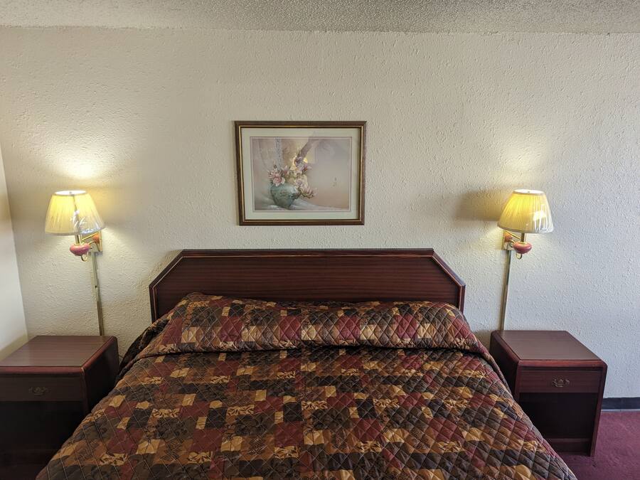 A bedroom with a wooden headboard, a quilted bedspread, two bedside tables with lamps, and a framed picture on the wall.