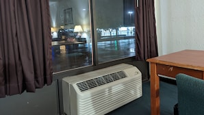 Una habitación con un ventanal grande, un calefactor portátil, una mesa y una silla.