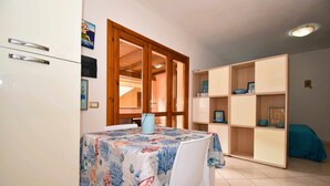 A room with a dining table covered with a tablecloth, a bookshelf, and a bed with a blue cover. - Well-finished studio apartment with A/C wifi and veranda (Aglientu)