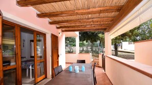 An outdoor patio with a wooden pergola, a dining table with chairs, and a view of the surrounding landscape. - Well-finished studio apartment with A/C wifi and veranda (Aglientu)