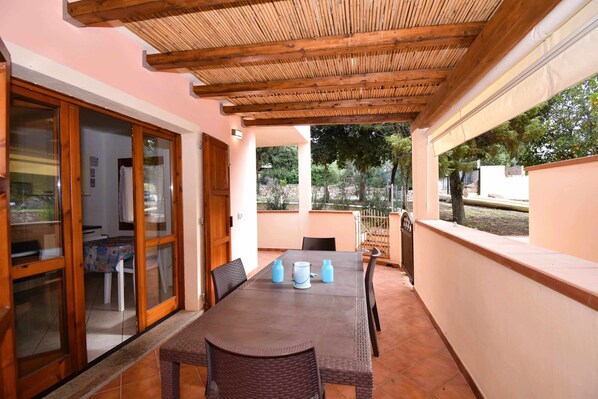 An outdoor patio with a wooden pergola, a dining table with chairs, and a view of the surrounding landscape.