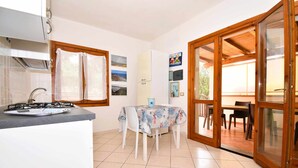 A kitchen with a gas stove, a dining table with chairs, and a sliding glass door leading to an outdoor area. - Well-finished studio apartment with A/C wifi and veranda (Aglientu)
