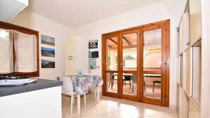 A kitchen with a dining table, chairs, and a view through a glass door to an outdoor area. - Well-finished studio apartment with A/C wifi and veranda (Aglientu)
