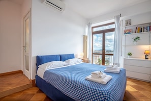 A bedroom with a bed, a window, a radiator, a shelf with books, and a plant.