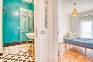 A room with a bed, a bathroom with a shower, a sink, and a window.