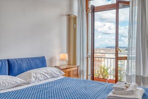 A hotel room with a bed, a nightstand, a lamp, a window with curtains, and a view of the city.