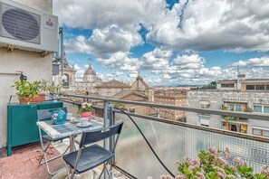 A balcony with a table, chairs, and potted plants.