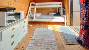 Et hyggeligt kabinrum med køjeseng, kommode med skuffer, fjernsyn og et vindue med gardiner.