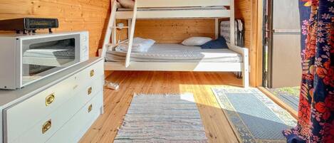 Acogedora habitación tipo cabaña con literas, cómoda con cajones, televisor y ventana con cortinas.