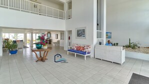 Een ruime lobby met een hoge plafond, een receptiebalie, een zithoek met een bank, en een groot raam.