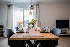 Un comedor con una mesa de madera, sillas, un florero con flores y un televisor al fondo.