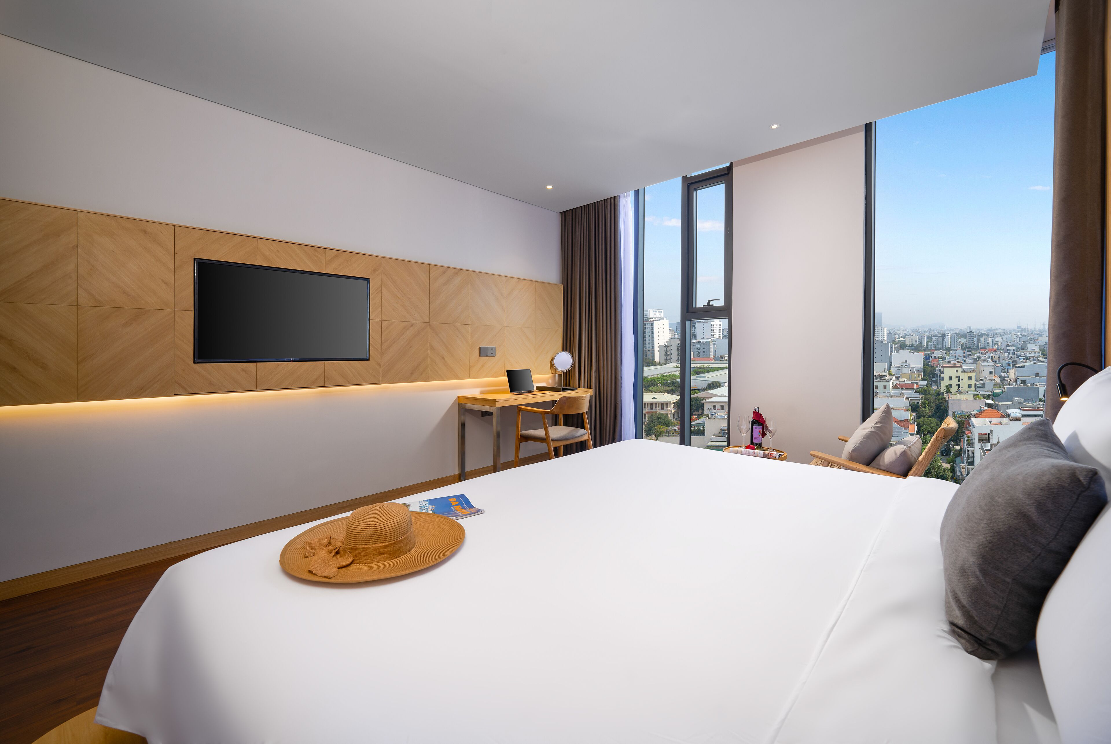 A modern hotel room with a large bed, a desk, a flat-screen TV, and a city view.