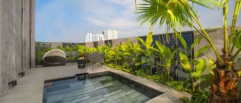 A rooftop pool with a modern design, surrounded by lush greenery and a cityscape view.