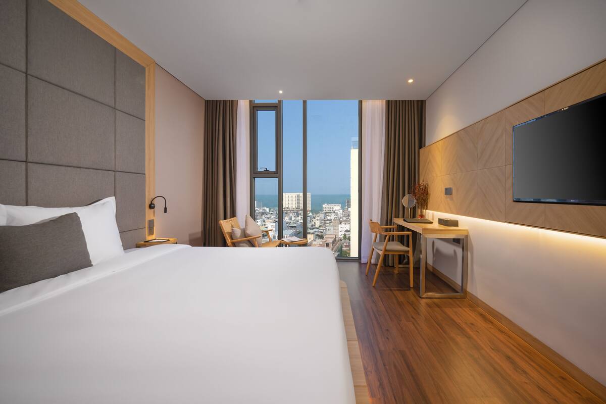 A modern hotel room with a large bed, a desk, and a TV.