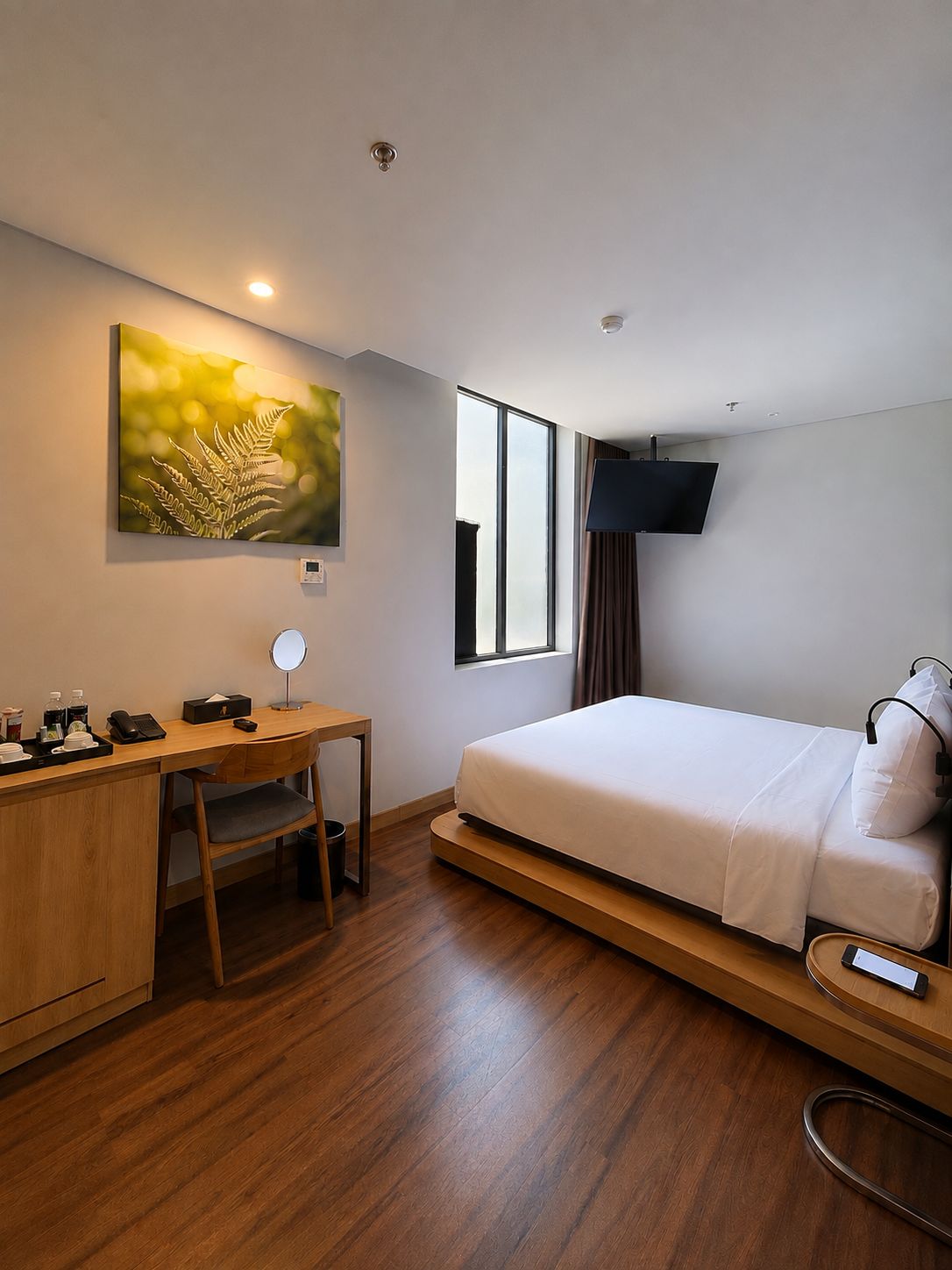A hotel room with a bed, a desk, a chair, a TV mounted on the wall, and a window.