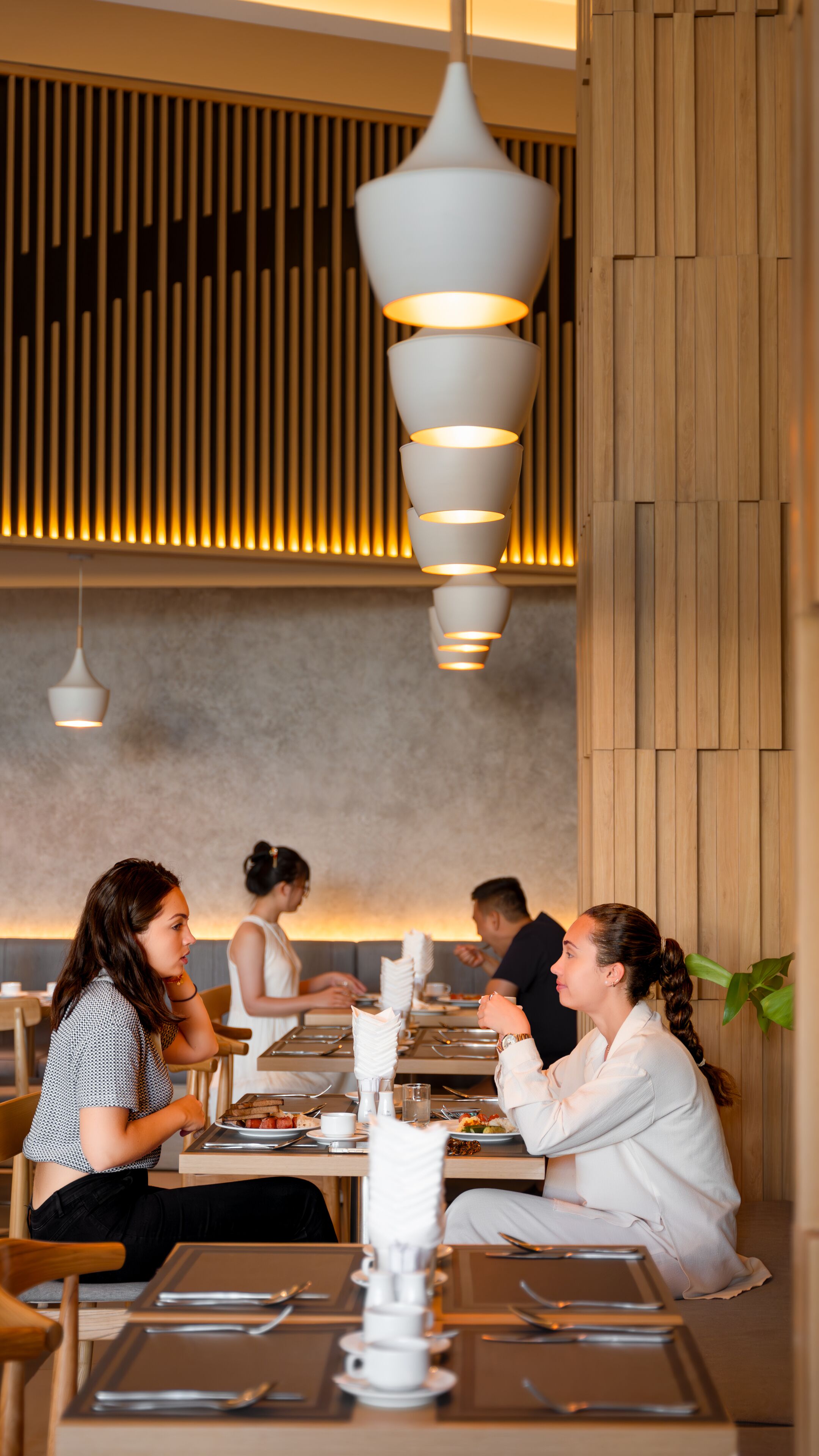 A restaurant interior with wooden paneling, modern pendant lighting, and diners seated at tables.