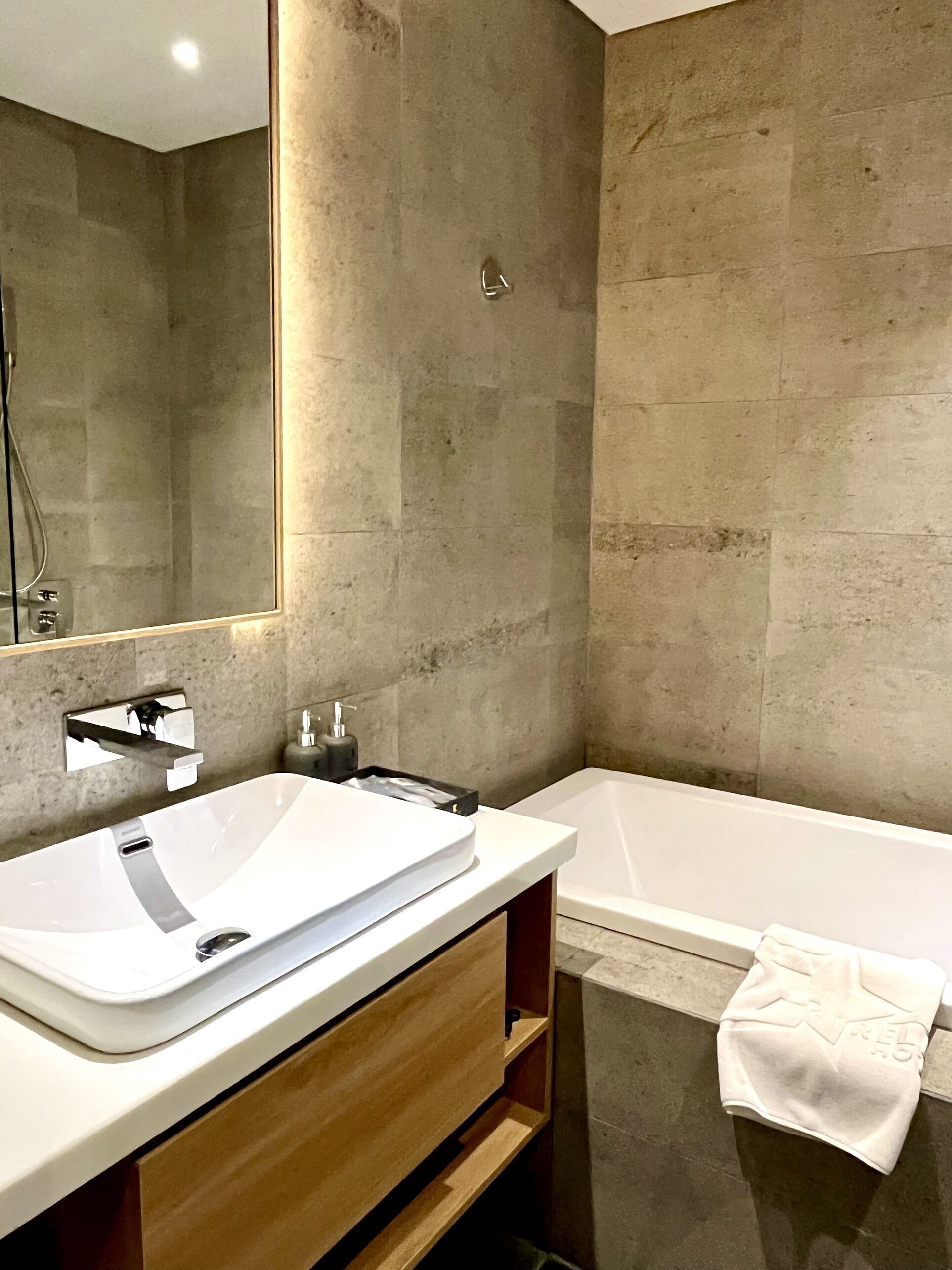 Une salle de bain moderne avec un grand miroir, un lavabo blanc et une baignoire.