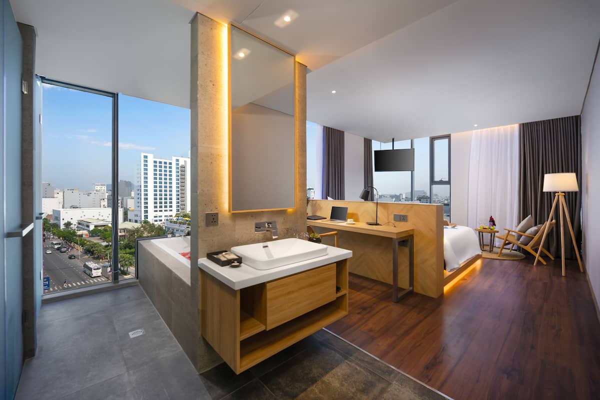 A modern hotel bathroom with a large mirror, two sinks, a wooden vanity, and a desk with a chair.