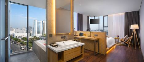 A modern hotel bathroom with a large mirror, two sinks, a wooden vanity, and a desk with a chair.
