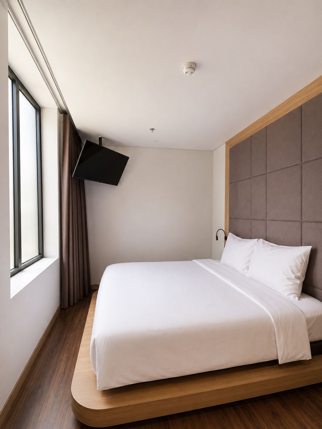 A modern hotel room with a bed, a mounted TV, and a window with curtains.