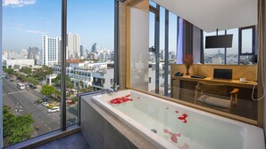 A modern bathroom with a large bathtub, a desk with a laptop, and a view of the city through large windows. - Estrella Boutique Hotel (Da Nang)