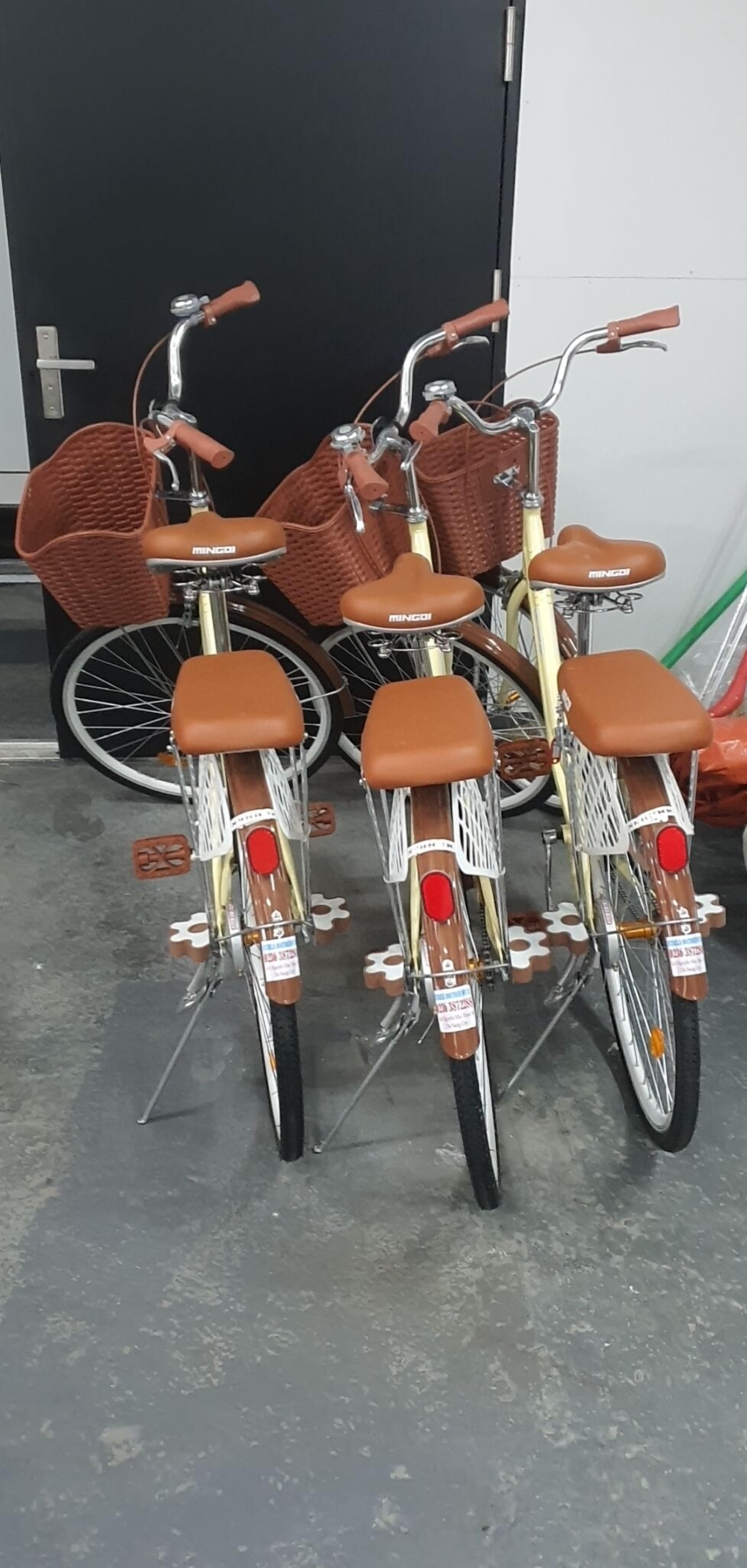 Three bicycles parked indoors with baskets and brown seats.