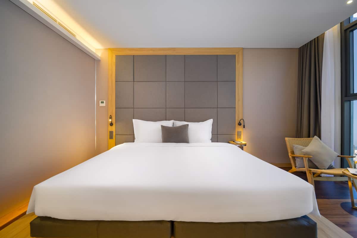 A large bed with white linens, a wooden headboard, and a nightstand with a lamp.