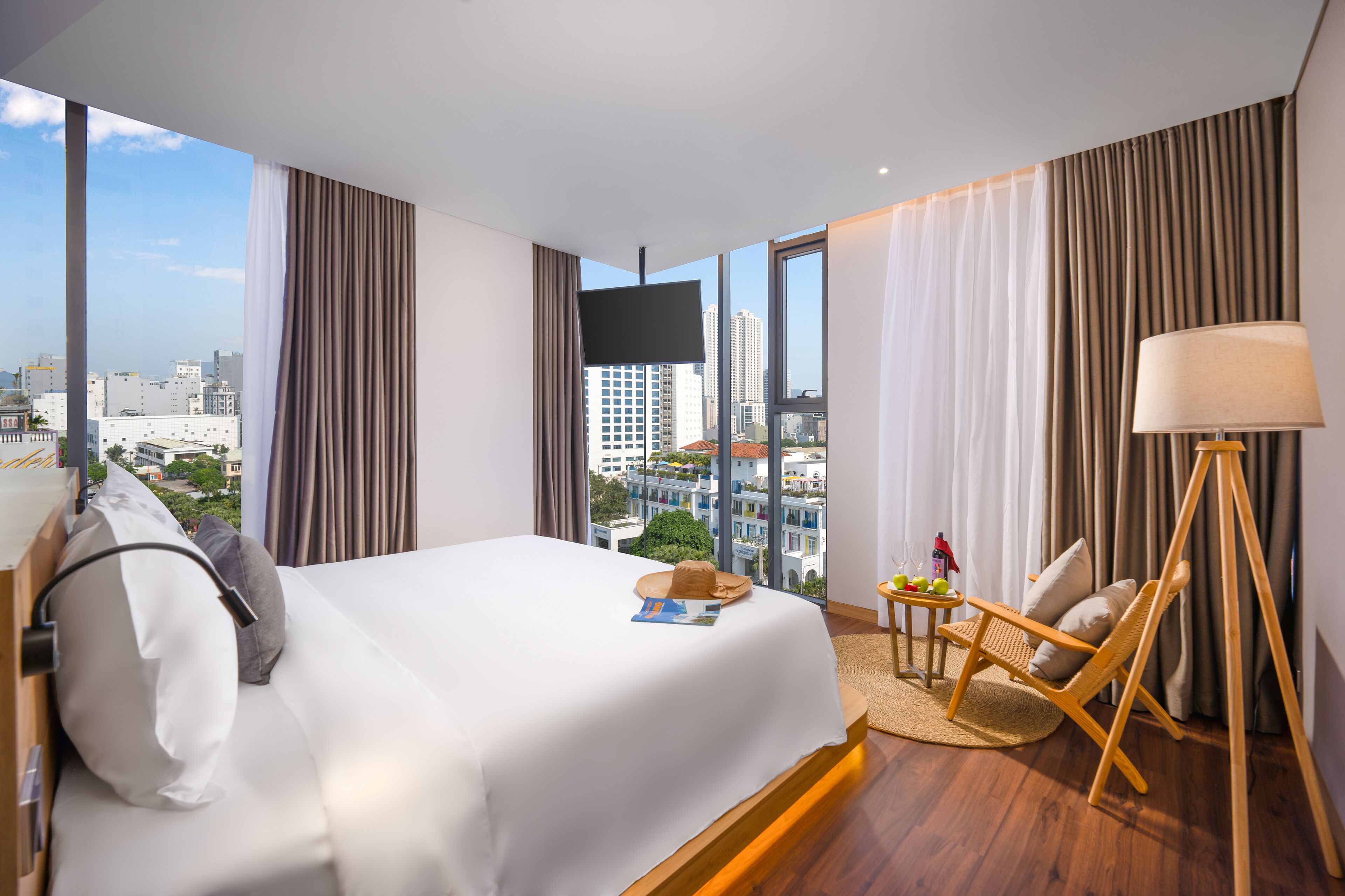 A modern hotel room with a large bed, a desk with a lamp, and a view of the cityscape.