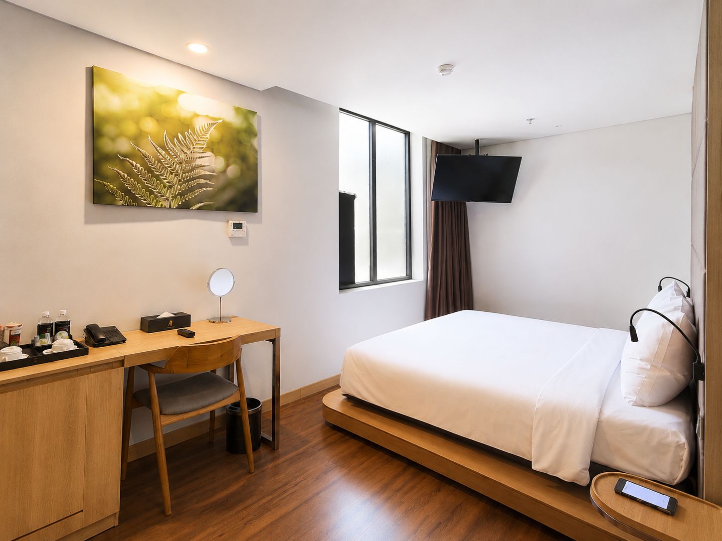 Ein Hotelzimmer mit einem Bett, einem Schreibtisch mit Stuhl, einem an der Wand befestigten Fernseher und einem Fenster mit Vorhängen.
