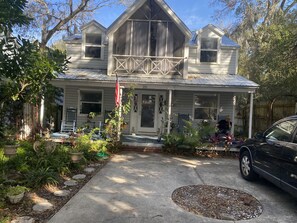 A two-story house with a porch, a flag, and a car parked in front.