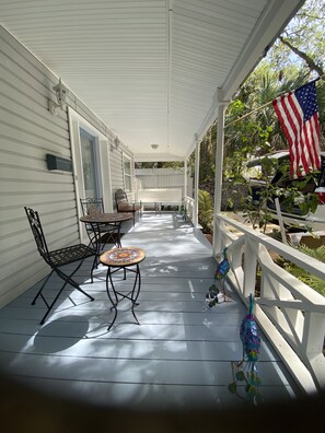 A covered porch with a table and chairs, an American flag, and a decorative bird.