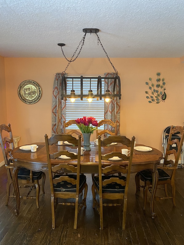 A dining room with a wooden table and chairs, a chandelier, and a window with blinds.