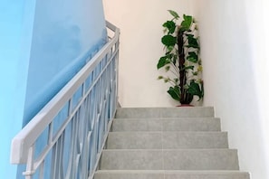 A staircase with a white railing, grey steps, and a potted plant on the right.