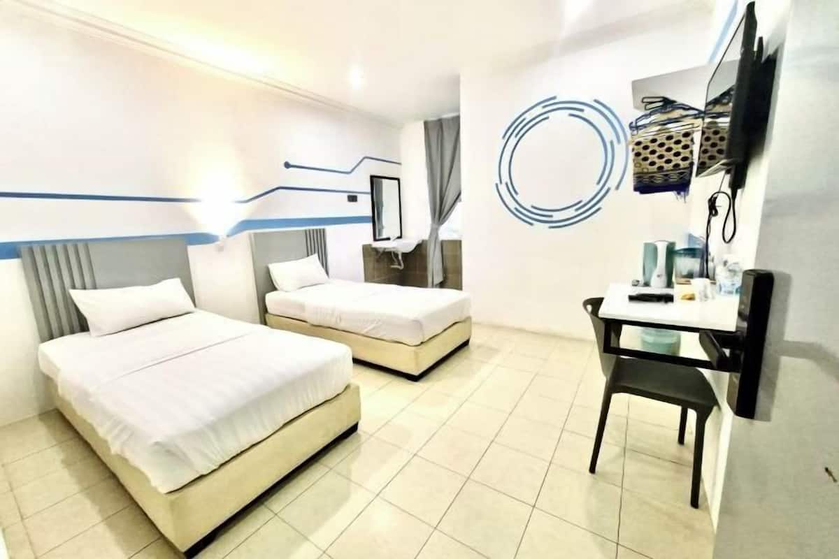 A hotel room with two beds, a desk, a chair, a TV, and a wall with abstract art.