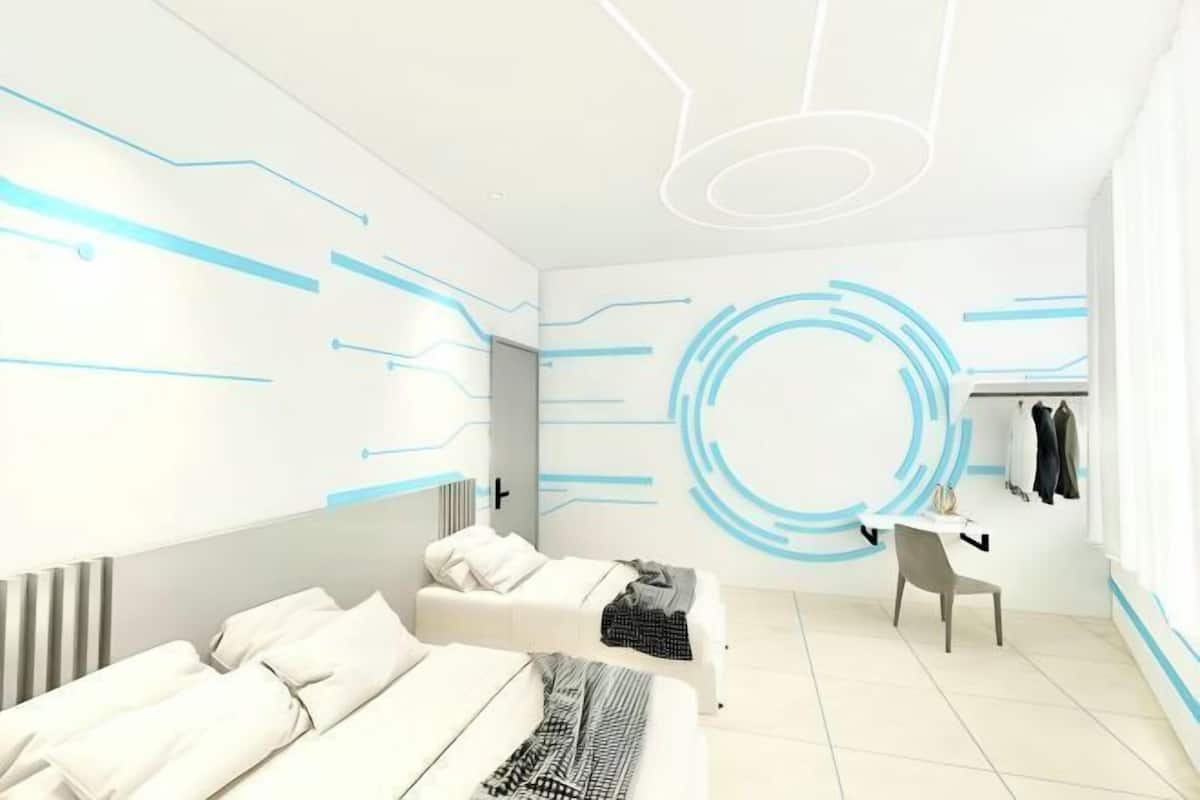 A modern hotel room with a minimalist design, featuring a bed, a desk, and a chair.