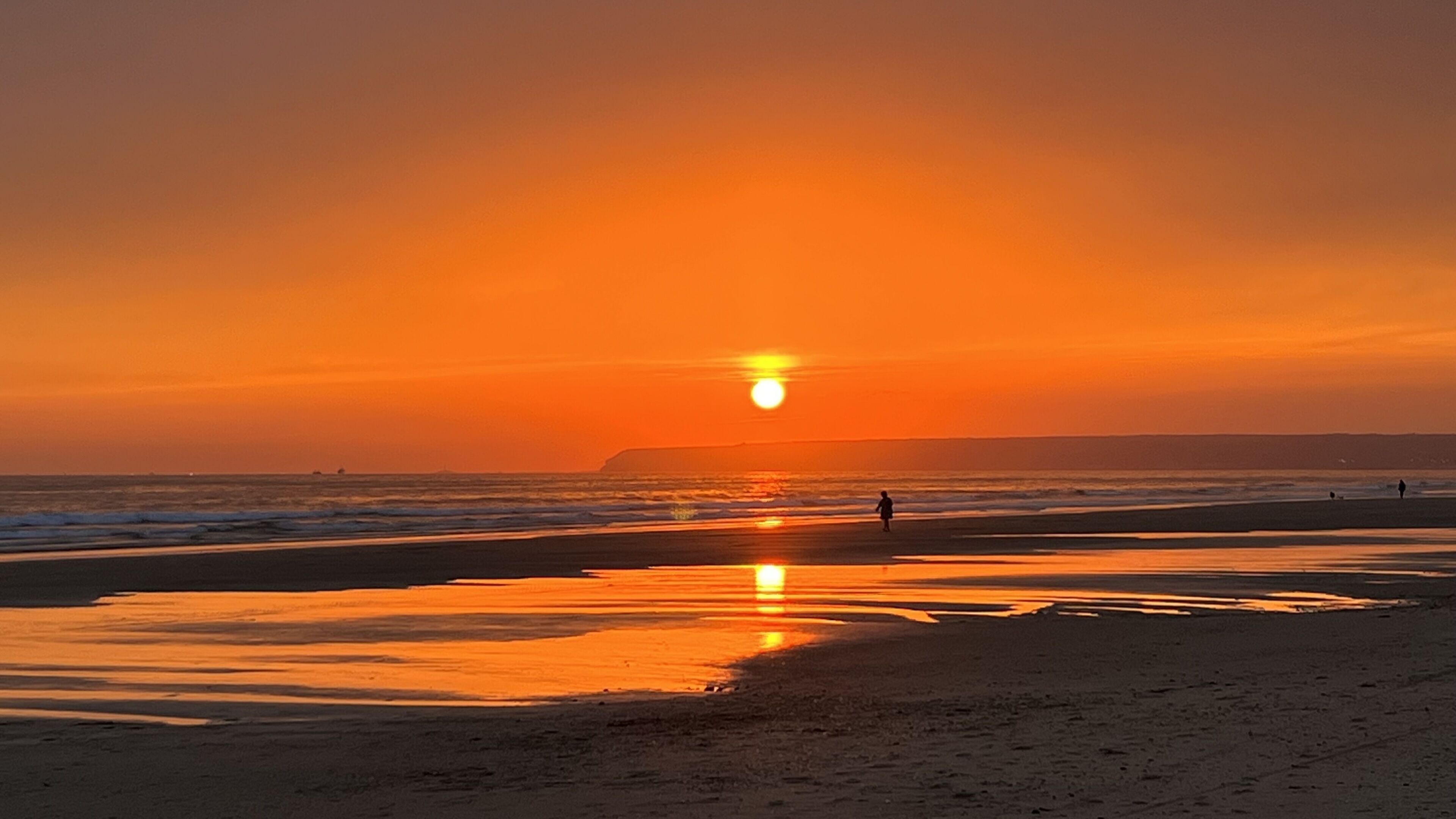 Escena de playa con atardecer, mar tranquilo y tierra a lo lejos.