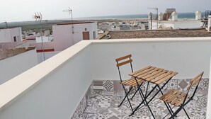A rooftop terrace with a table and chairs, patterned floor tiles, and a view of the sea and buildings in the distance. - Junquera Apartment in Conil (Conil)