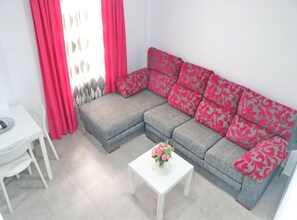 Un salon comprenant un canapé d’angle gris, une table basse blanche agrémentée d’un arrangement floral et une table à manger blanche avec des chaises.