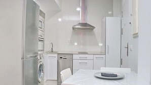 A modern kitchen with a stainless steel refrigerator, dishwasher, and oven. There is a dining table with chairs and a remote control on it. - Junquera Apartment in Conil (Conil)