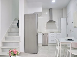 Une cuisine moderne avec des meubles blancs, un réfrigérateur en acier inoxydable, un lave-vaisselle et un coin repas comprenant une table et des chaises.