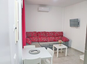 Un petit salon moderne avec un canapé gris, des meubles blancs et un téléviseur à écran plat fixé au mur.