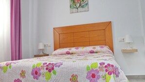 A bedroom with a wooden headboard, a floral bedspread, a nightstand with a lamp, and a wall-mounted power outlet. - Junquera Apartment in Conil (Conil)