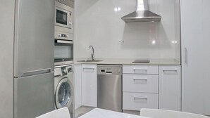 A modern kitchen with a built-in oven, microwave, dishwasher, and a stainless steel range hood. - Junquera Apartment in Conil (Conil)