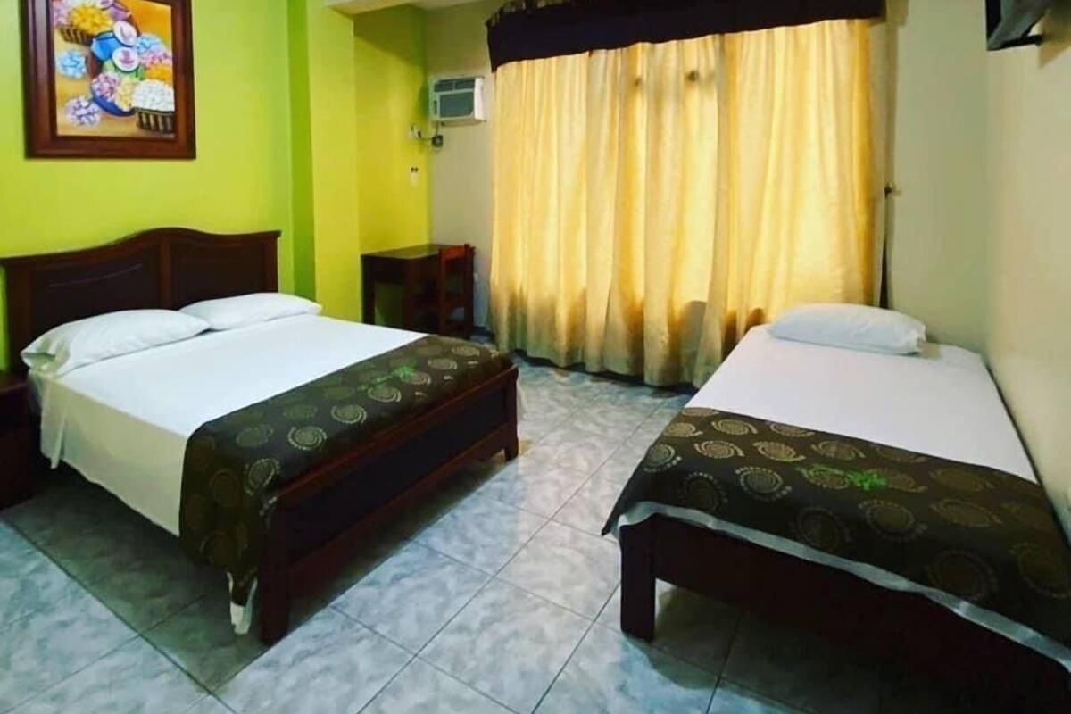 A hotel room with two beds, a painting on the wall, an air conditioning unit, and a curtain.