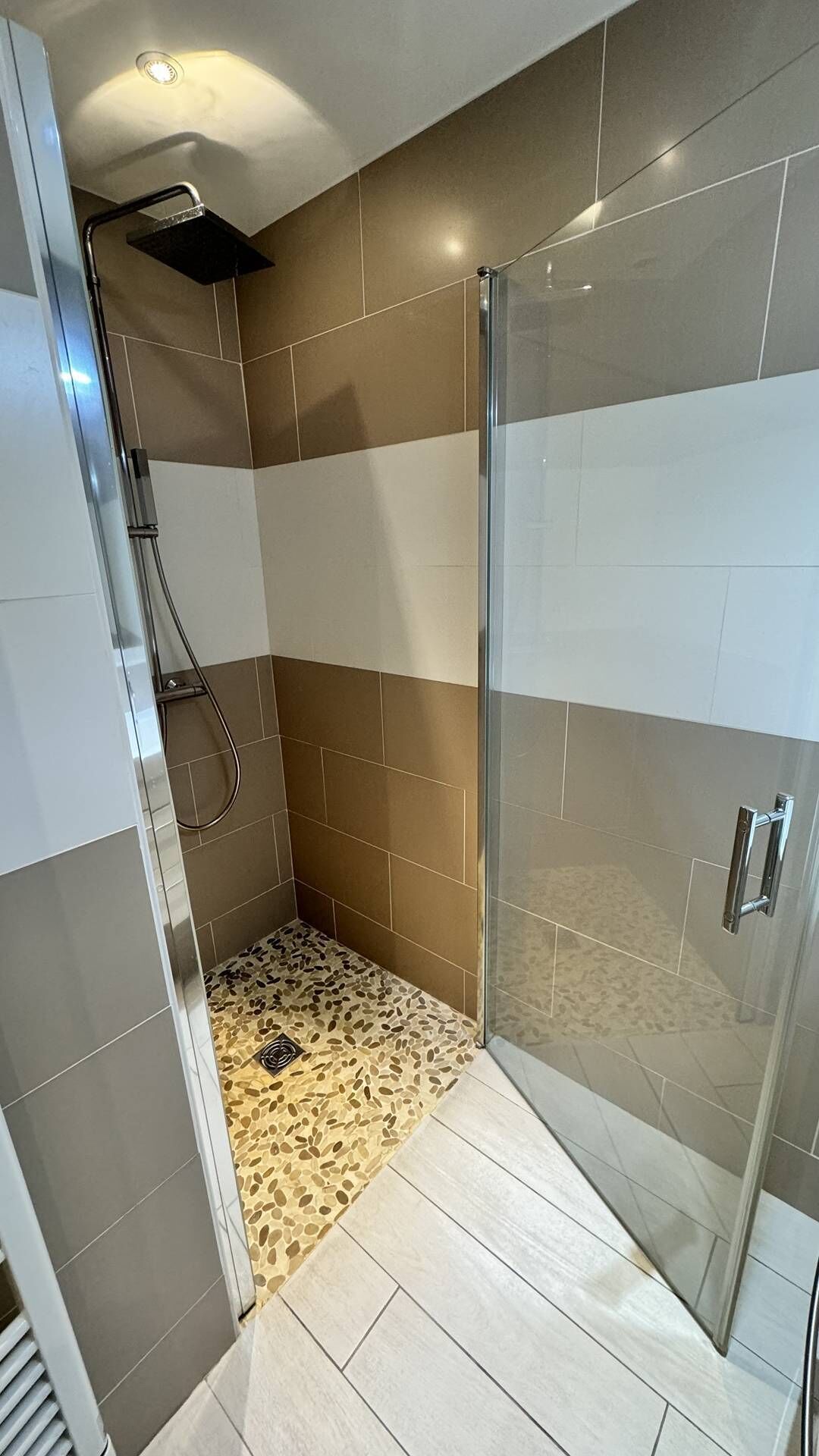 Une douche moderne avec une porte en verre, des carreaux beiges et blancs, et un sol à motifs.