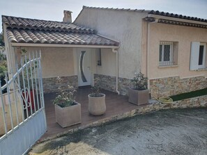 Una casa con techo de tejas, porche cubierto y base de piedra.
